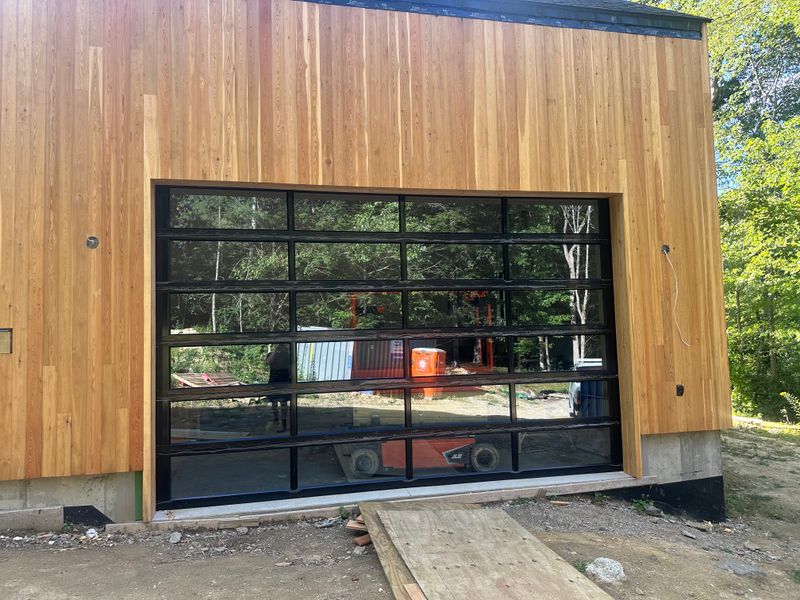 Full-view aluminum and glass garage door installed on modern cedar building